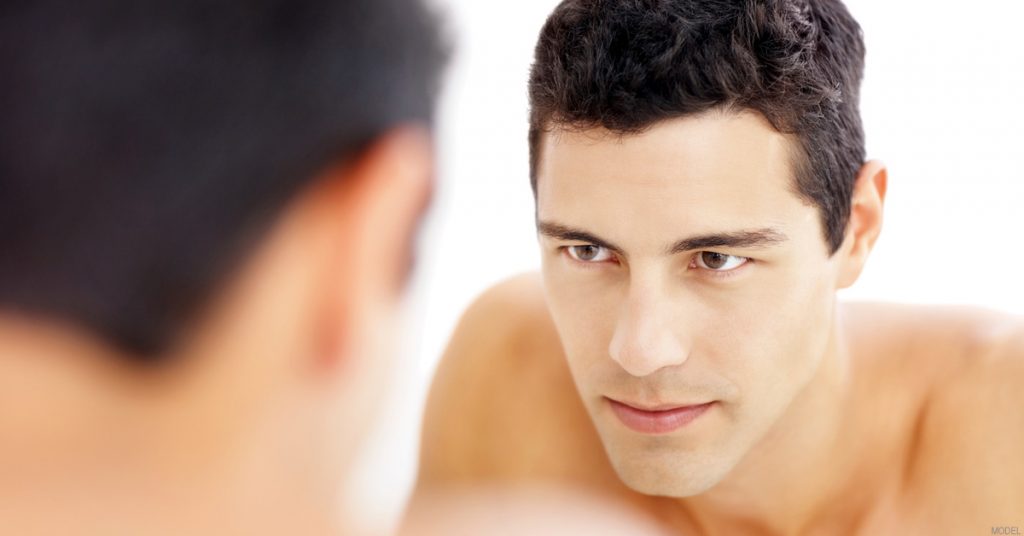 Confident man looking at his ears in the mirror after ear surgery.