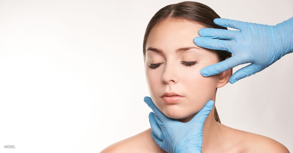 A woman's face being touched by a doctor's hands in gloves (MODEL)