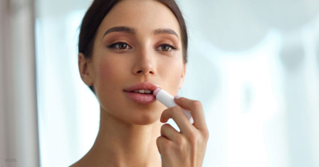 A young woman looking in the mirror and applying lipstick (MODEL)